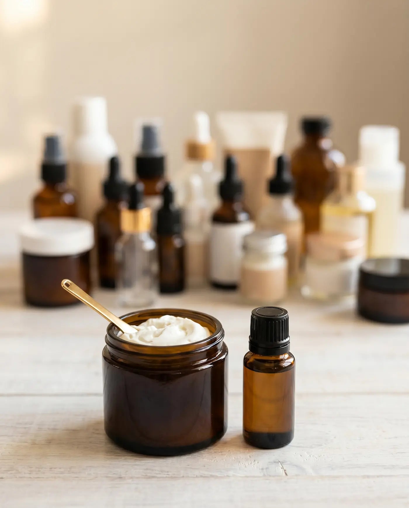 Open jar of whipped grass-fed tallow next to an amber essential oil bottle on a wooden counter, with assorted unused ingredient bottles softly blurred behind.