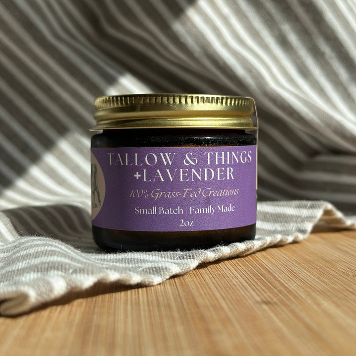 A jar of Tallow &amp; Things Lavender skin tallow balm placed on a wooden surface with a cloth in the background. The label on the jar reads &