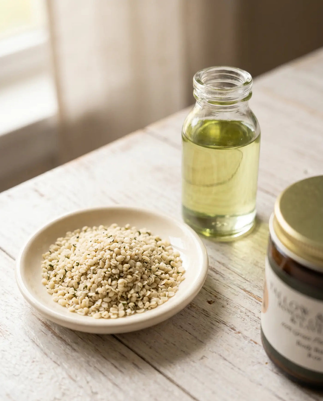 Amber jar of Tallow & Things Roman Chamomile & Lavender Body Butter beside refined hemp seed oil and hulled hemp seeds on a wood surface.