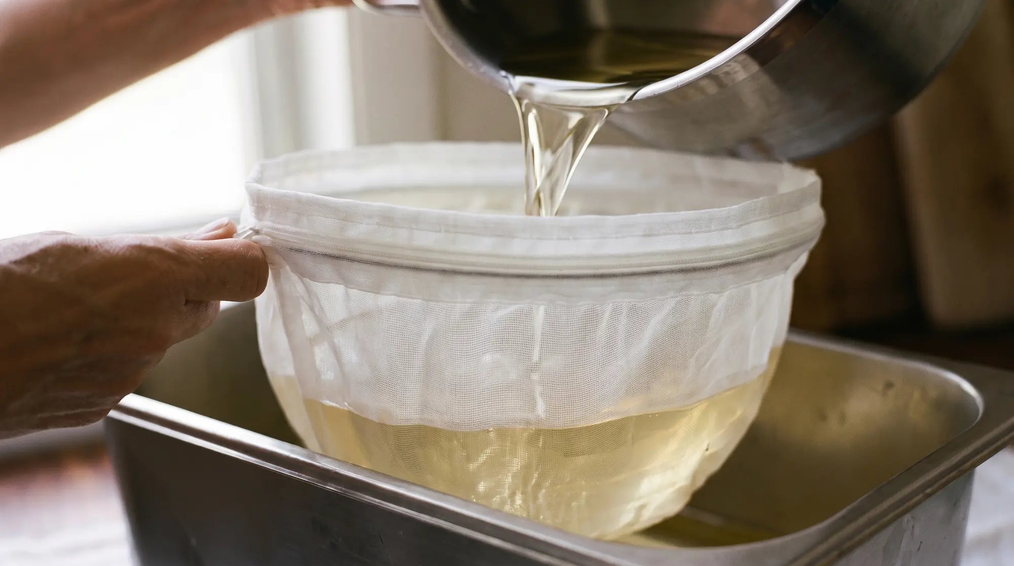 Golden grass-fed tallow being strained through fine mesh during the rendering process.