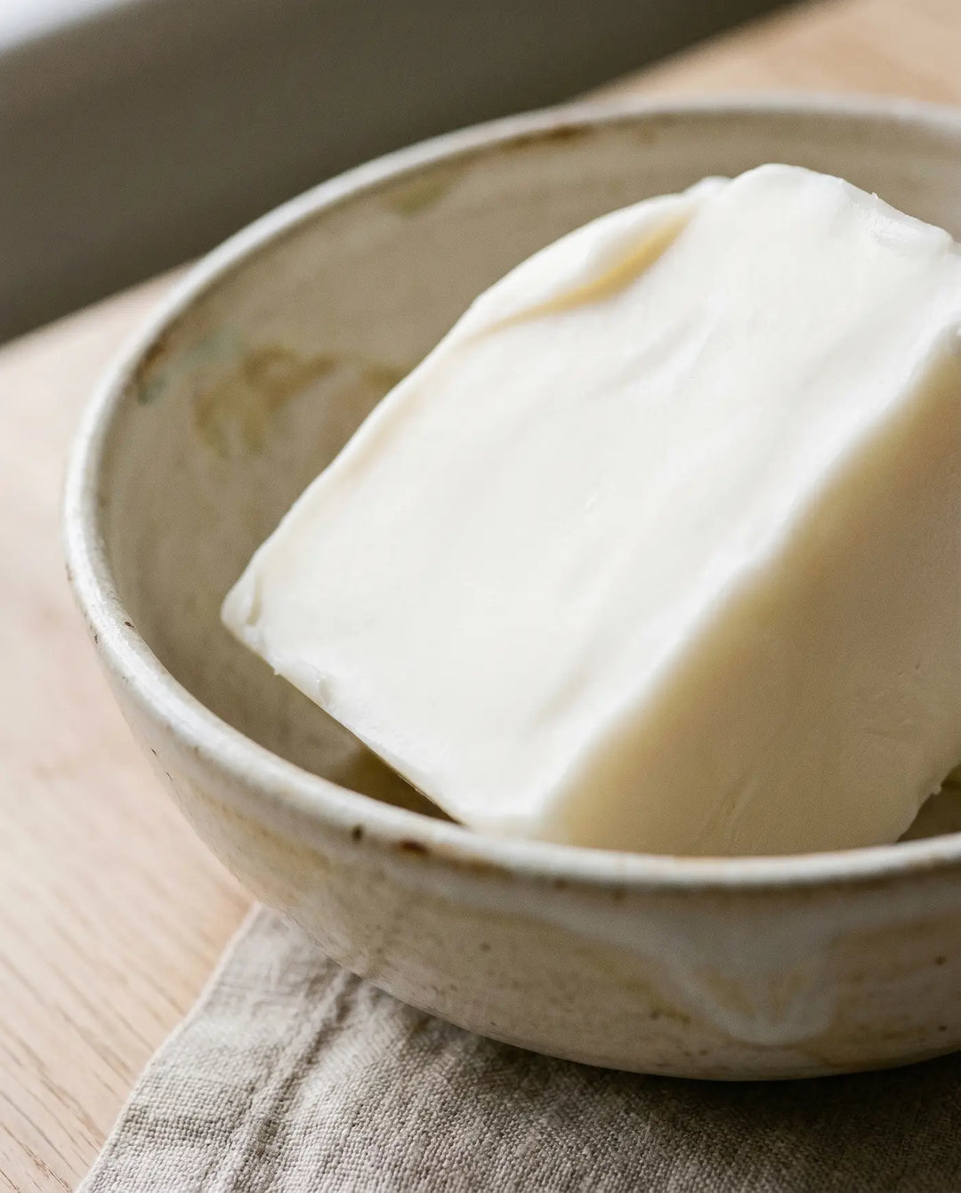 A smooth block of cosmetic-grade rendered tallow in a stoneware bowl