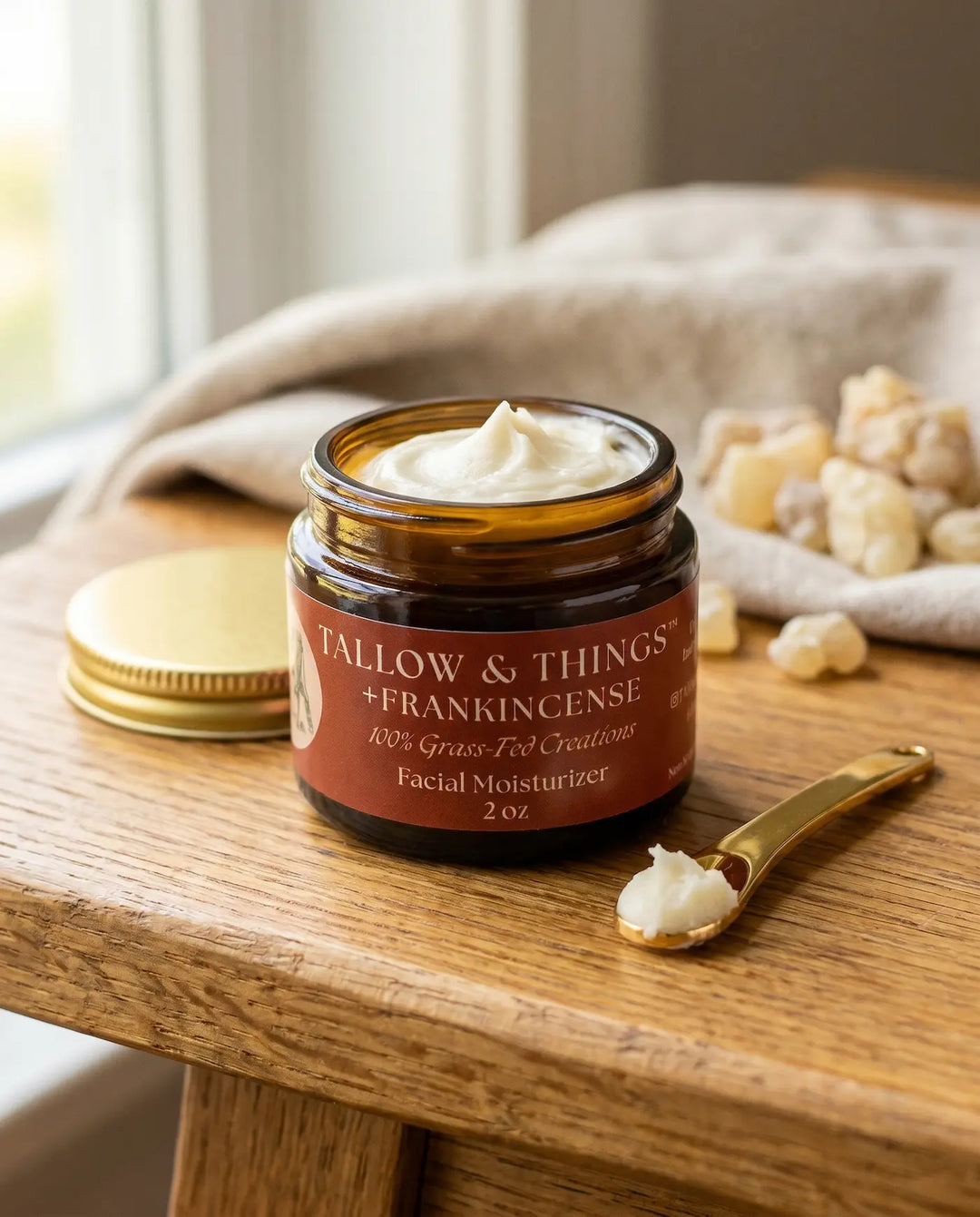 Open jar of Tallow & Things frankincense facial moisturizer with a small gold spoon scooping whipped cream.