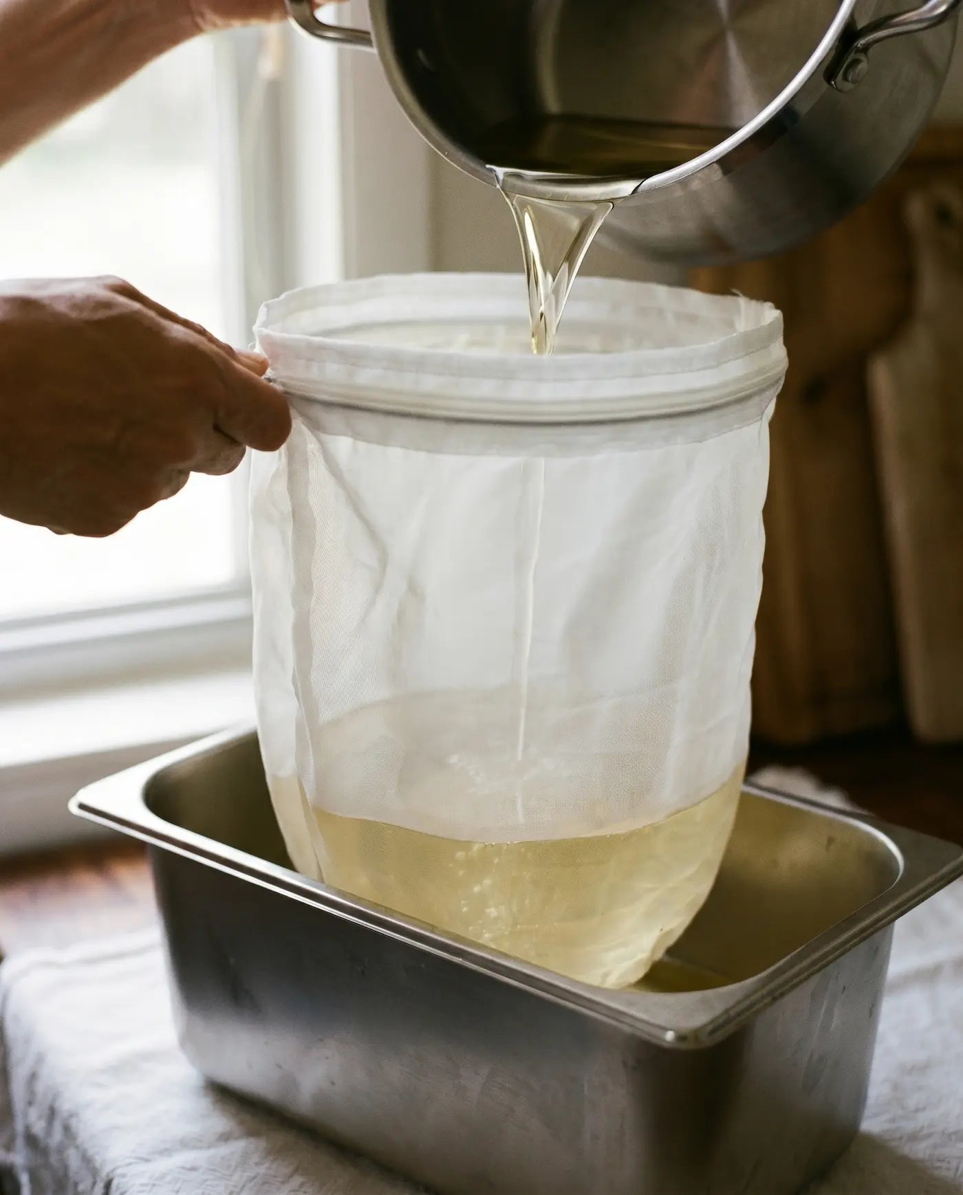 Golden liquid tallow being strained through a fine mesh filter into a stainless pan
