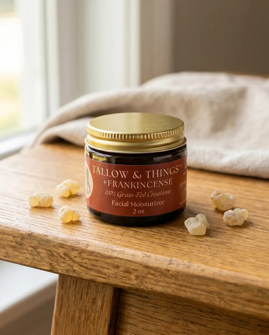 Frankincense facial moisturizer jar with golden resin on a wood table in soft window light.