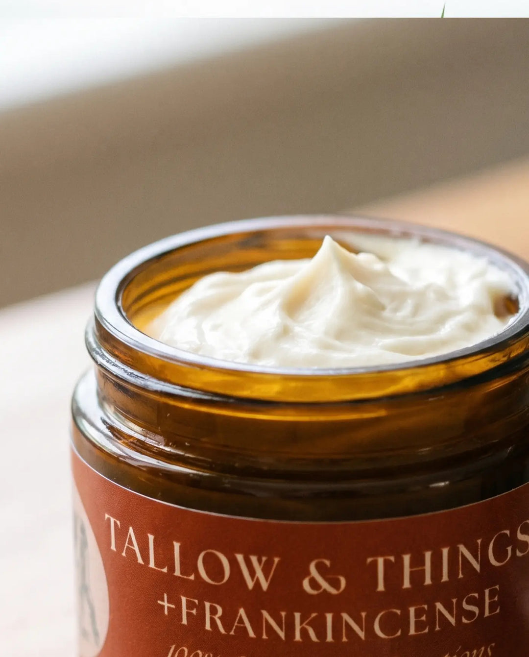 Open jar of frankincense tallow facial moisturizer showing whipped ivory cream in soft window light.