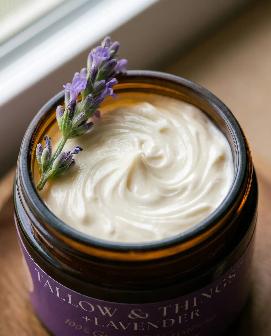 Close-up of whipped ivory lavender tallow moisturizer with a sprig of fresh lavender on the jar rim.