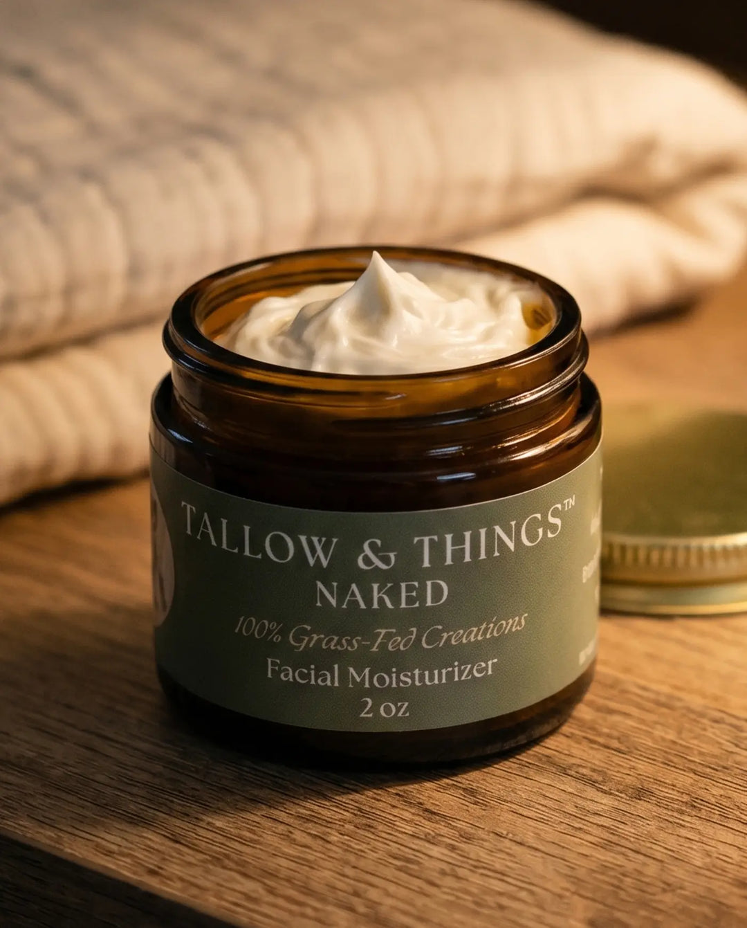 Naked facial moisturizer jar open on a nightstand in warm evening lamplight beside a folded blanket.