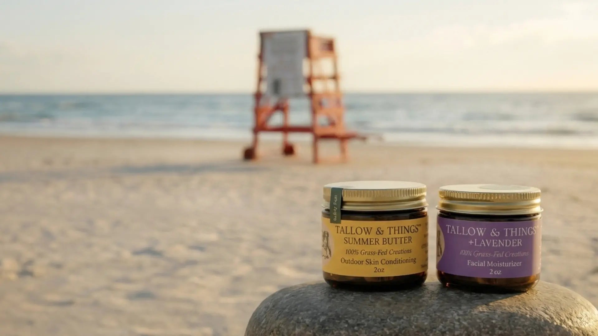 Tallow & Things Summer Butter and Lavender jars on a rock at the beach with a lifeguard stand