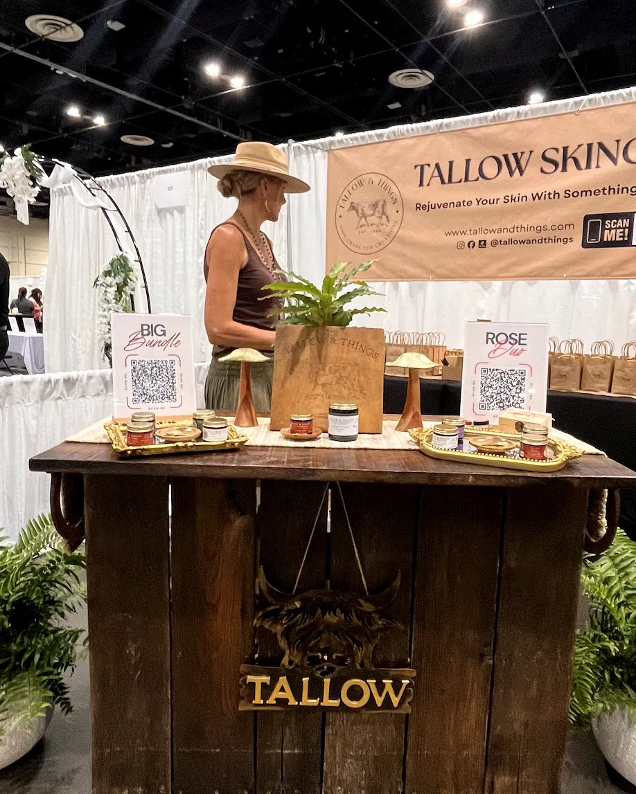Tallow and Things booth at an expo with a rustic wood counter, branded sign, and product display.